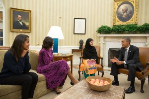 United States President Barack Obama (right), First Lady Michelle Obama (second from left), and their daughter Malia (left) meet with Malala Yousafzai (second from right), a young Pakistani schoolgirl who was shot in the head by the Taliban in 2012, in the Oval Office on 11 October 2013. Image Credit: White House/WikiMedia