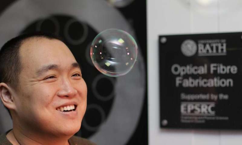 The fiber's long and thin bubbles of glass reflect light into the fiber's core much in the same way that light reflects off the surface of the soap bubble in the foreground, making it appear iridescent. Credit: University of Bath