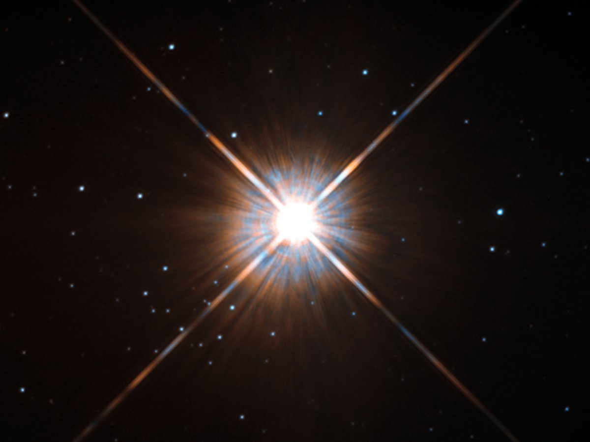 Shining brightly in this Hubble image is our closest stellar neighbour: Proxima Centauri. Proxima Centauri lies in the constellation of Centaurus (The Centaur), just over four light-years from Earth. Although it looks bright through the eye of Hubble, as you might expect from the nearest star to the Solar System, Proxima Centauri is not visible to the naked eye. Its average luminosity is very low, and it is quite small compared to other stars, at only about an eighth of the mass of the Sun. However, on occasion, its brightness increases. Proxima is what is known as a “flare star”, meaning that convection processes within the star’s body make it prone to random and dramatic changes in brightness. The convection processes not only trigger brilliant bursts of starlight but, combined with other factors, mean that Proxima Centauri is in for a very long life. Astronomers predict that this star will remain middle-aged — or a “main sequence” star in astronomical terms — for another four trillion years, some 300 times the age of the current Universe. These observations were taken using Hubble’s Wide Field and Planetary Camera 2 (WFPC2). Proxima Centauri is actually part of a triple star system — its two companions, Alpha Centauri A and B, lie out of frame. Although by cosmic standards it is a close neighbour, Proxima Centauri remains a point-like object even using Hubble’s eagle-eyed vision, hinting at the vast scale of the Universe around us.