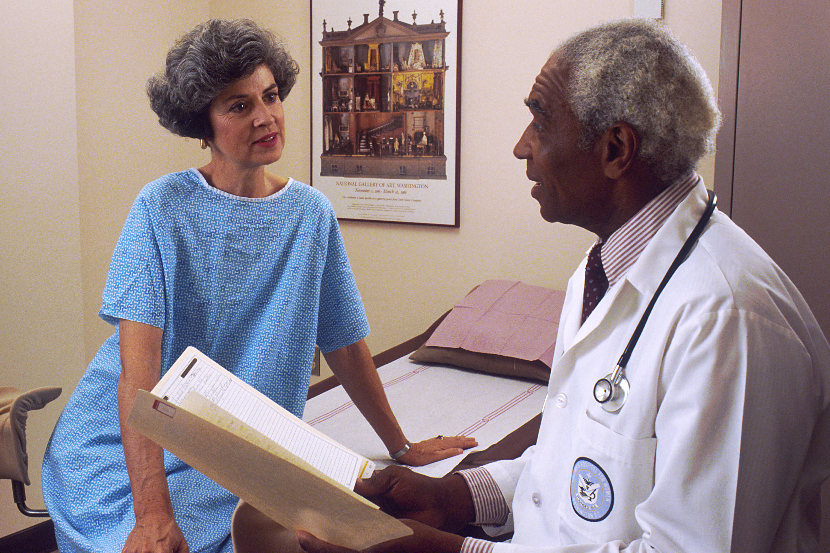 A black older male doctor consults with a white female patient in a hospital room, which should be standard in clinical trials.
