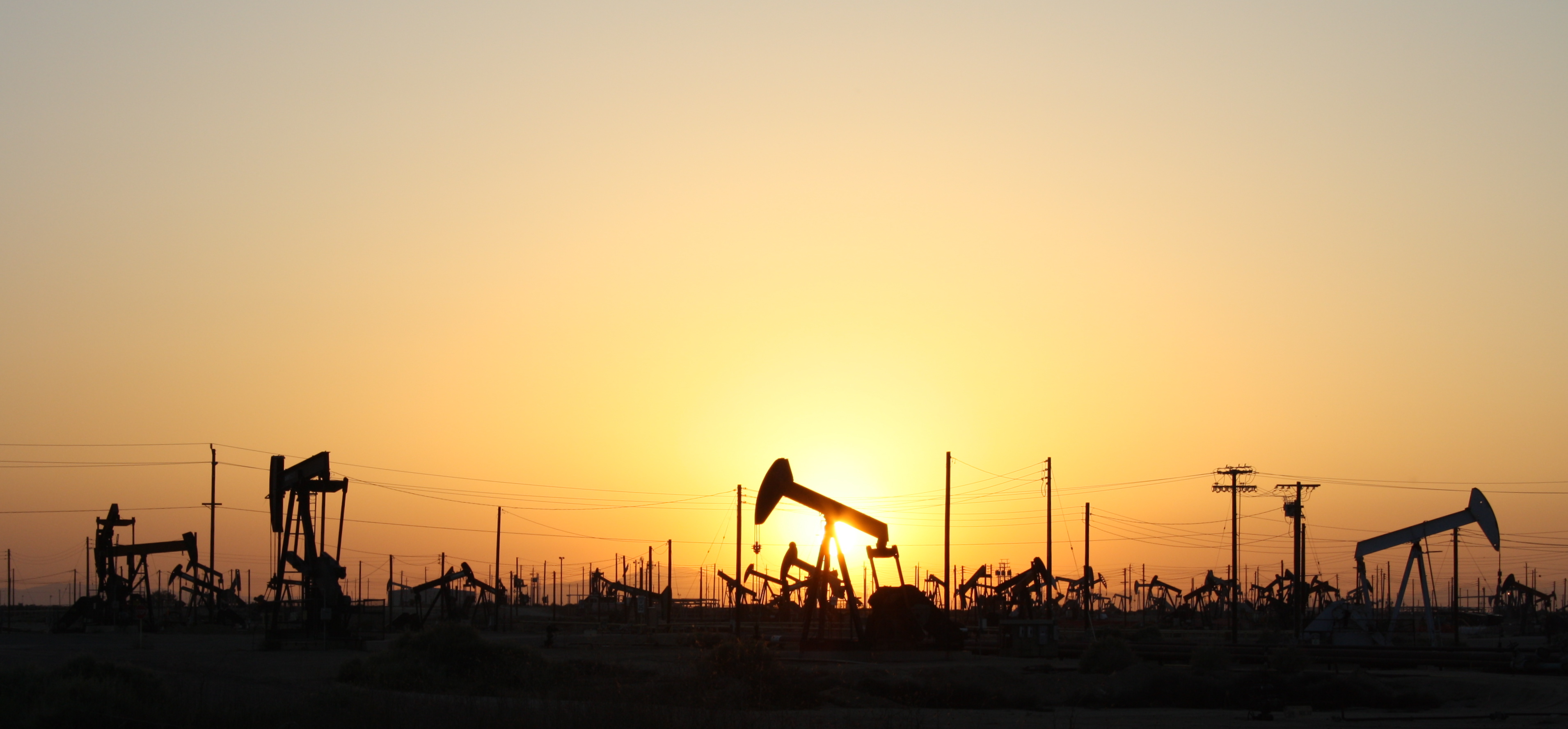 A field of pumpjacks in an oil field, a common source of methane, backlit by a sunset.