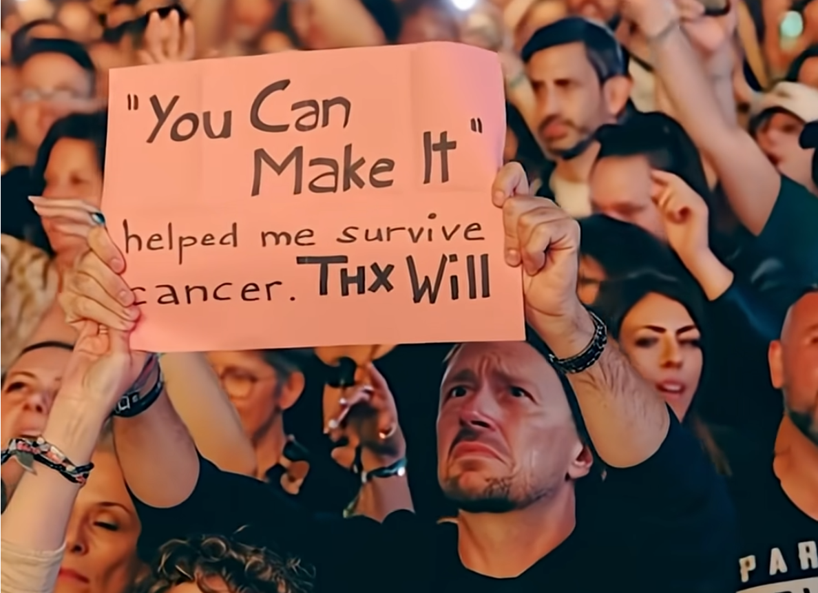 A man with a wildly exaggerated facial expression holding a sign that says "'You Can Make It' helped me survive cancer. Thx Will"