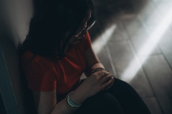 Upset teen girl sit on floor sadly look out window worried about teenage problem at school and communication with parent. Worried girl tensely suffer about bullying at school, unrequited love with boy
