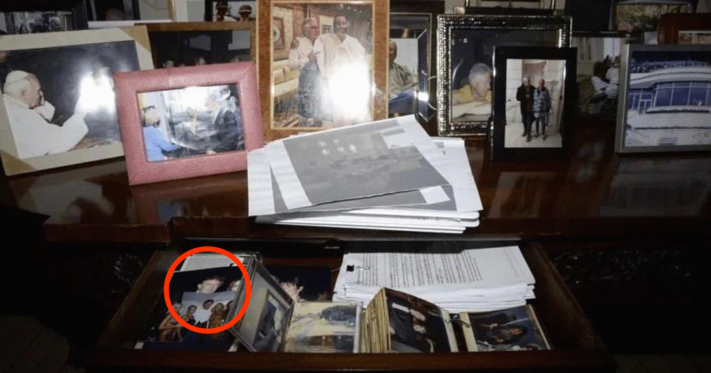 Image showing framed photographs on what appears to be a desk. One photo in the bottom left, inside an open drawer, appears to show Donald Trump's face.