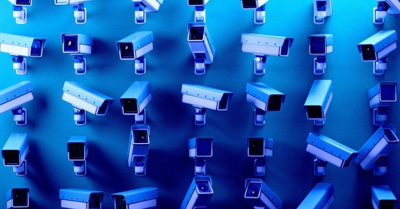 Multiple white security cameras mounted on a blue wall, arranged in a grid pattern, all facing different directions. The image has a blue tint, giving it a cool, technological atmosphere.