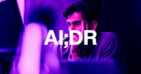 A man with dark curly hair resting his face on his hand, looking thoughtful or concerned, illuminated by purple and pink lighting. The large white text "AI;DR" is overlaid across the center of the image.