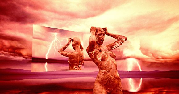 A surreal scene featuring a metallic, copper-colored female figure with a textured surface, holding her head with both hands. Behind her is a large reflective mirror showing her back and a lightning strike in the background. The sky is filled with dramatic, reddish-orange clouds, and the ground appears reflective, mirroring the intense sky and lightning.