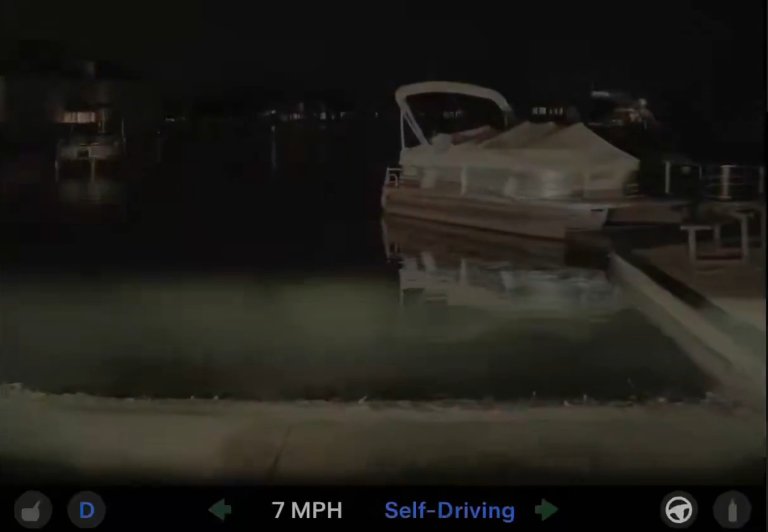 Still frame from video by Tesla driver Daniel Milligan. A boat docked at a pier at night, with its reflection visible in the calm water. The image is taken from a vehicle dashboard camera, showing a speed of 7 MPH and indicating that the vehicle is in self-driving mode.
