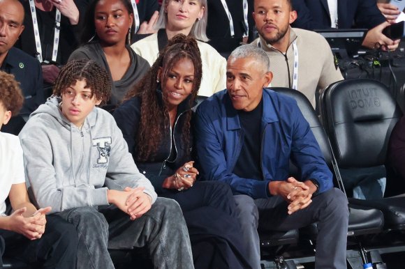 Barack Obama and Michelle Obama seated in a sports stadium.