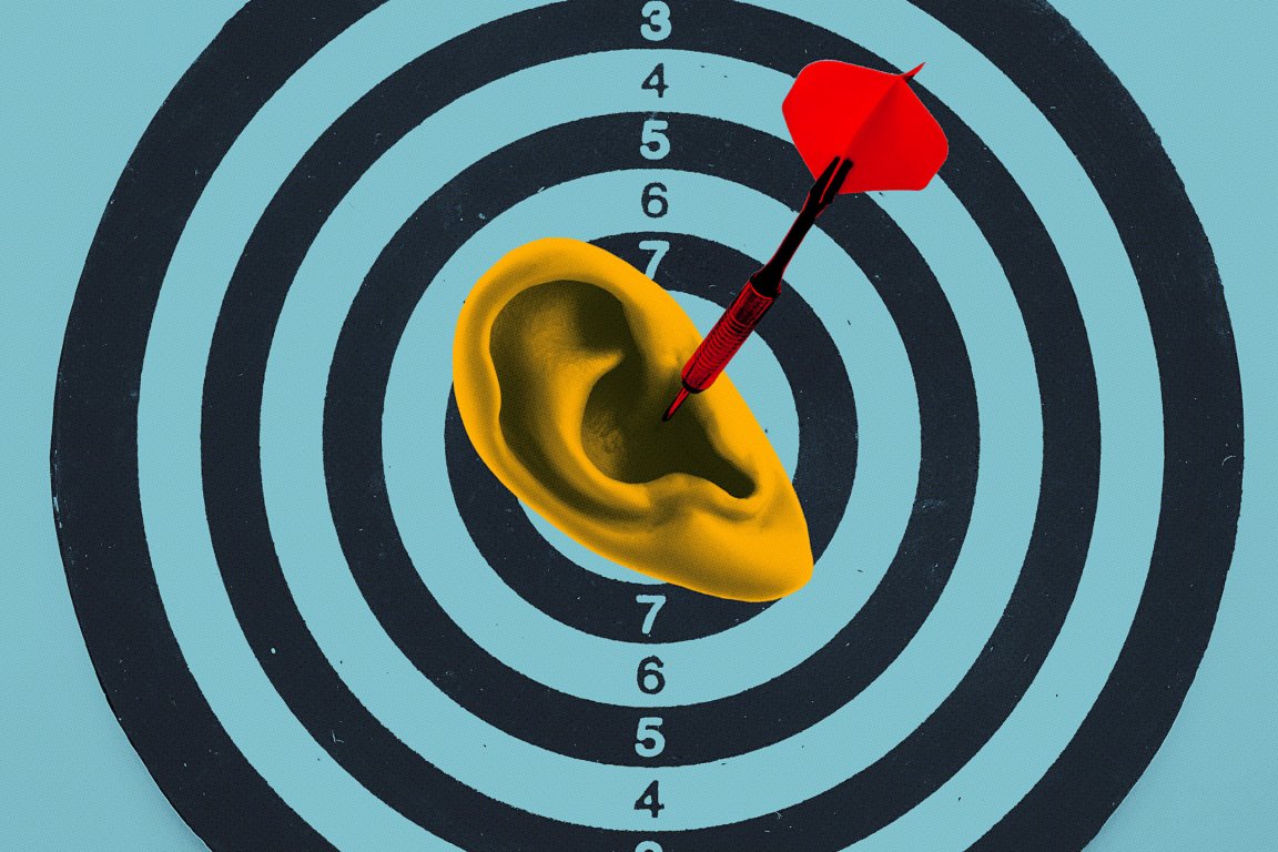 A red dart is stuck in the center of a yellow human ear, which is placed on a black and blue target board with concentric circles and numbers.