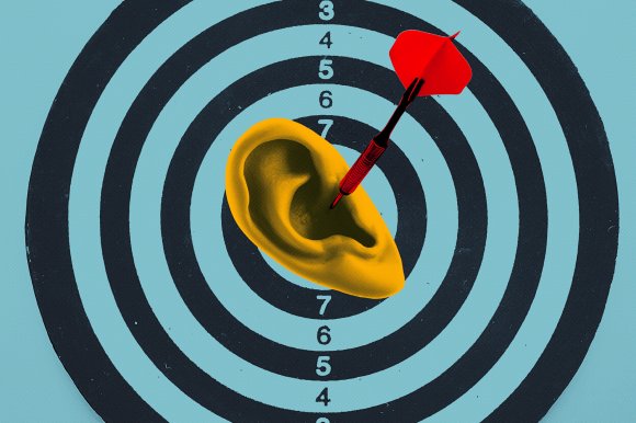 A red dart is stuck in the center of a yellow human ear, which is placed on a black and blue target board with concentric circles and numbers.