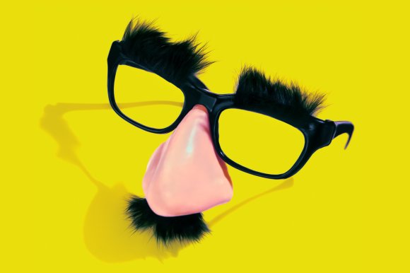 Black novelty glasses with attached bushy black eyebrows, a large pink fake nose, and a small black mustache, set against a bright yellow background.