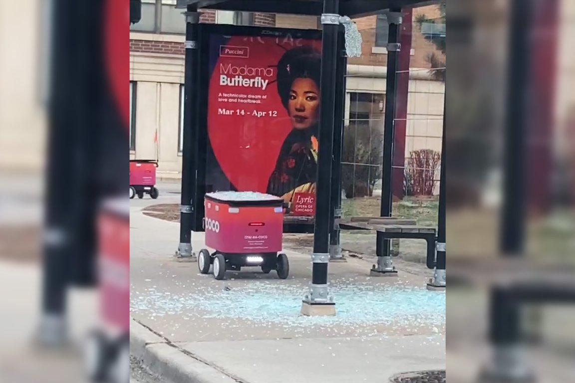 A small red delivery robot with the label "COCO" is at a bus stop with shattered glass scattered on the ground around it. Behind the robot, there is a poster advertising Puccini's opera "Madama Butterfly," showing a woman in traditional attire with the dates Mar 14 - Apr 12. The bus stop has black metal poles and a bench.