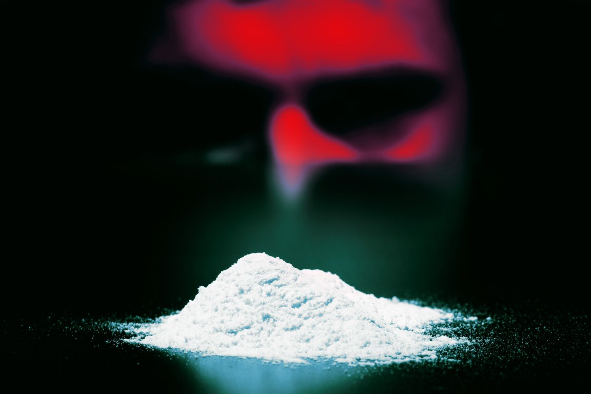 A small mound of fine white powder on a dark surface with a blurred red and black face in the background.