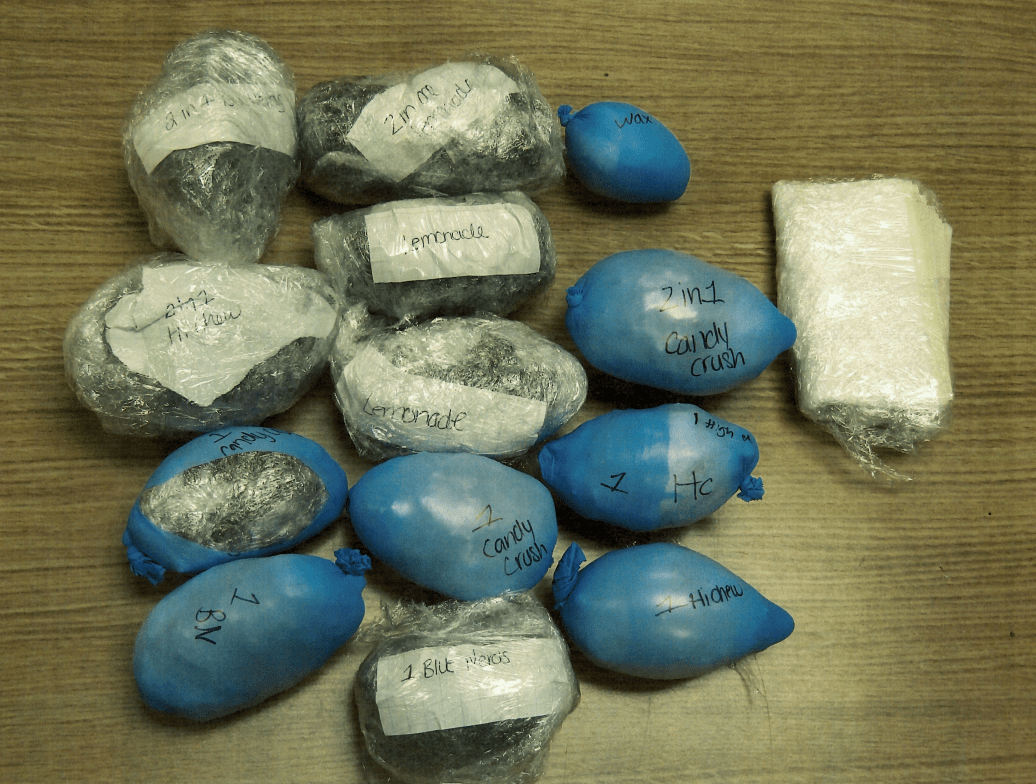 Thirteen lumpy balloons labeled with different strains of marijuana, next to a stack of papers in plastic wrap.