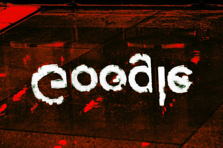 Reflection of the word "Google" in white paint on a wet, dark surface with red lighting accents. The letters appear distorted due to the water's ripples.