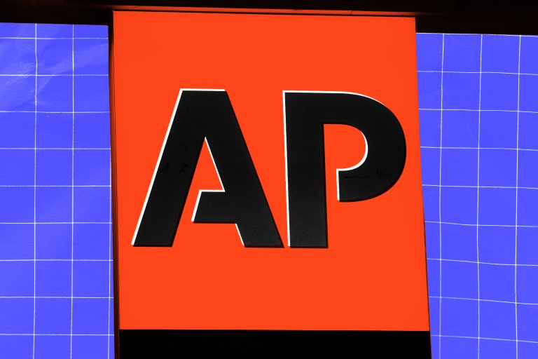 A close-up of a sign with a bright orange background featuring the large black letters "AP" outlined in white. The sign is flanked by blue panels with a white grid pattern.