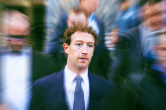 Mark Zuckerberg wearing a dark suit, white shirt, and dark tie, with a blurred background of people and a radial blur effect centered on his face.