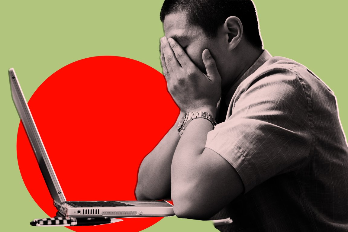 A man sitting at a desk with a laptop in front of him, covering his face with both hands, appearing stressed or overwhelmed. The background features a large red circle on a light green backdrop. The man is wearing a short-sleeved shirt and a wristwatch.