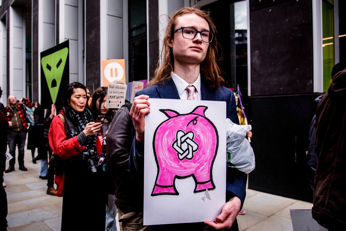 A young person holds a sign at a protest against OpenAI.