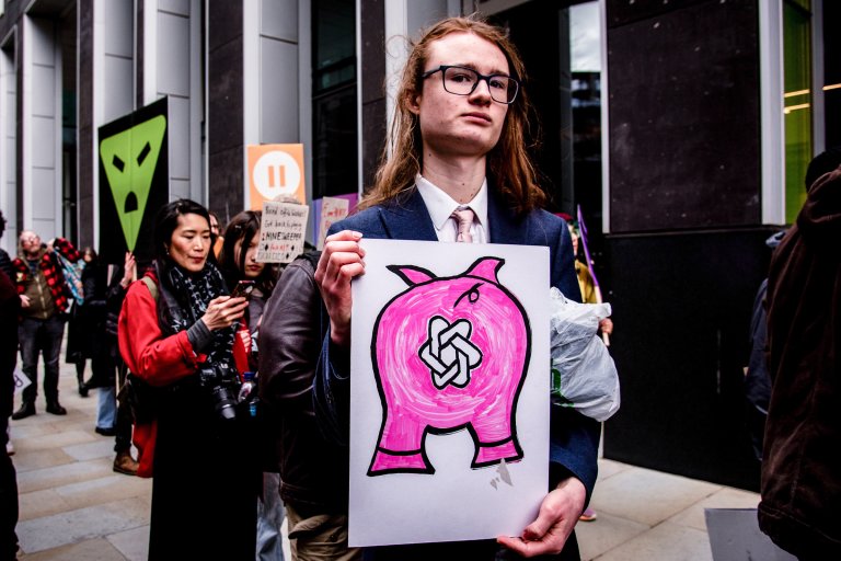 A young person holds a sign at a protest against OpenAI.