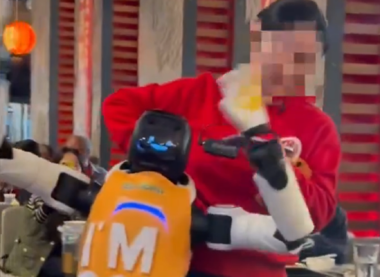 A person in a red jacket is grabbing a robot while it dances out of control.