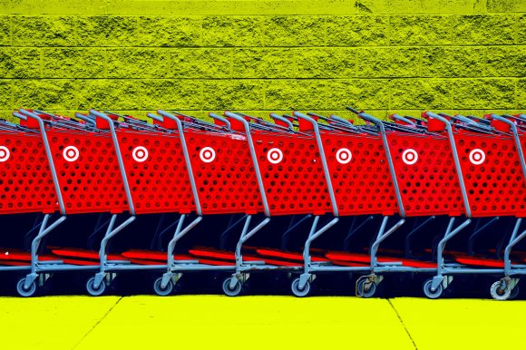 A row of red Target shopping carts lined up side by side against a textured yellow brick wall and yellow ground. The carts have the distinctive white Target logo on their sides.