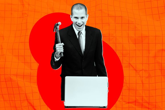A man in a black suit and tie is holding a hammer in his right hand, raised near his shoulder, and standing behind a laptop. The man is smiling with an open mouth. The background features an orange grid pattern with a large red abstract shape behind him. The man and laptop are in black and white, contrasting with the colorful background.