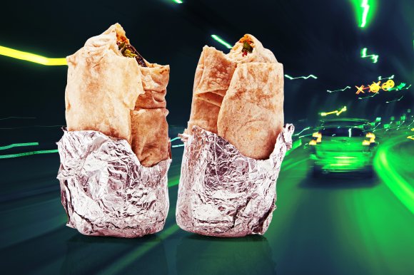 Two partially unwrapped burritos with foil at the bottom, set against a blurred background of a car driving through a tunnel with green and yellow lights.