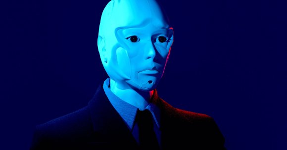 A humanoid robot with a smooth, pale blue face and black eyes, dressed in a dark suit, shirt, and tie, set against a deep blue background with subtle red lighting on one side of the face.