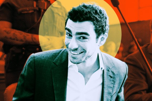 Luigi Mangione is depicted smiling broadly. He is wearing a dark suit jacket over a white shirt. The image has a stylized, high-contrast effect with a yellow circular background behind his head and an orange and black textured background.