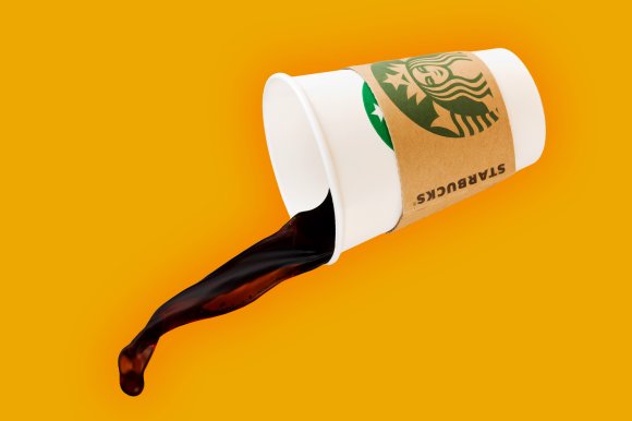 A white Starbucks paper cup with a brown sleeve is tipped over, spilling dark coffee against a solid orange background.