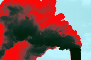 A large industrial smokestack emitting thick, dark smoke into the sky. The smoke has been digitally altered with a red overlay, creating a striking contrast against the light blue sky.