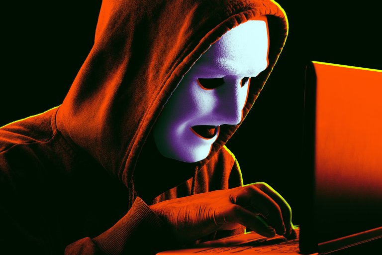 Person wearing a white mask and an orange hooded sweatshirt, typing on a laptop keyboard in a dark environment with dramatic orange and green lighting.