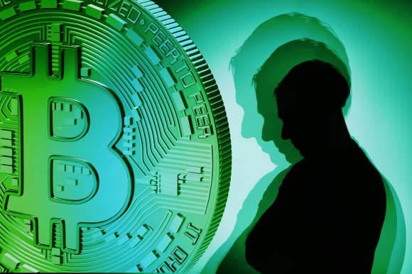 A large green and blue Bitcoin symbol on the left side, with a silhouette of a person on the right side casting multiple shadows against a green background. The image conveys a digital or cryptocurrency theme.