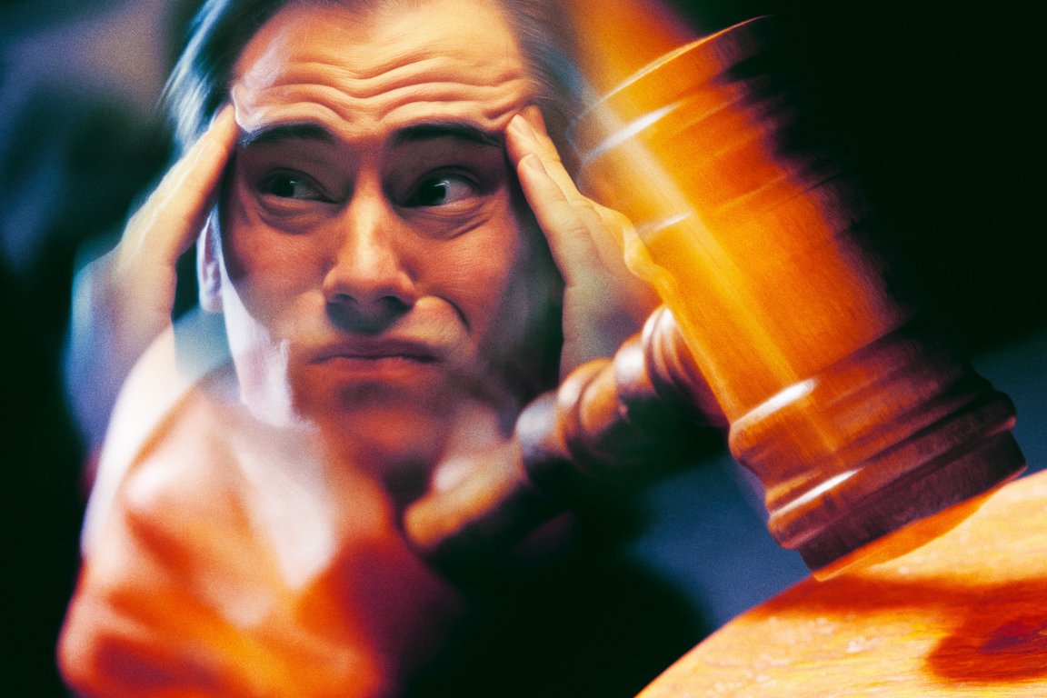 A man with a distressed expression holds his temples with both hands while a wooden judge's gavel is striking a surface in the foreground, creating a motion blur effect. The scene conveys tension or stress related to a legal or judicial situation.