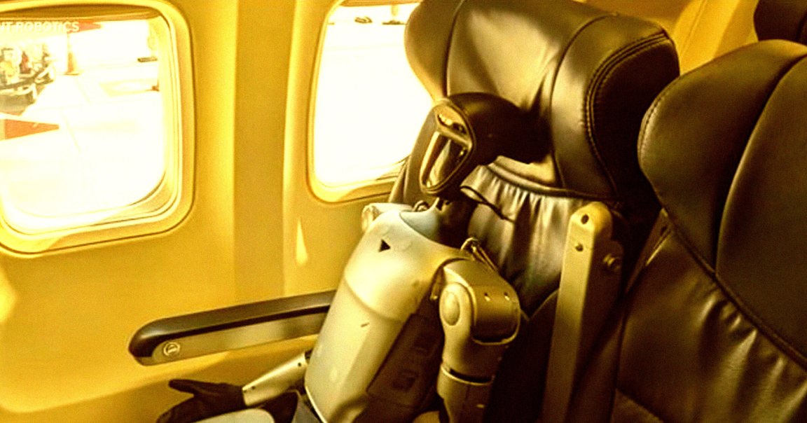 A humanoid robot is seated in an airplane window seat with black leather upholstery. The robot has a sleek, metallic body with a black head featuring a visor-like face. The airplane window shows a bright, sunlit exterior.
