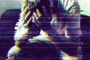 A person sitting with their head in their hands, appearing distressed or overwhelmed. The image has a glitch effect with horizontal digital distortion and color separation, giving it a fragmented and intense visual style. The person is wearing a light-colored shirt and has short hair.