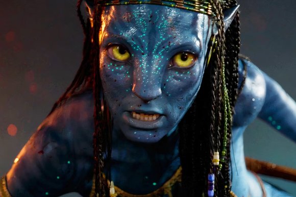 Close-up of a blue-skinned Na'vi character from the movie Avatar, with bright yellow eyes, bioluminescent spots on the face, braided hair adorned with beads, and an intense expression.