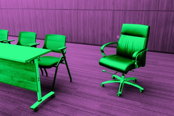 A modern office setting with a wooden table and three mesh-back chairs on one side, and a black leather executive swivel chair with armrests on the other side. The floor is carpeted, and the background features wood-paneled walls.