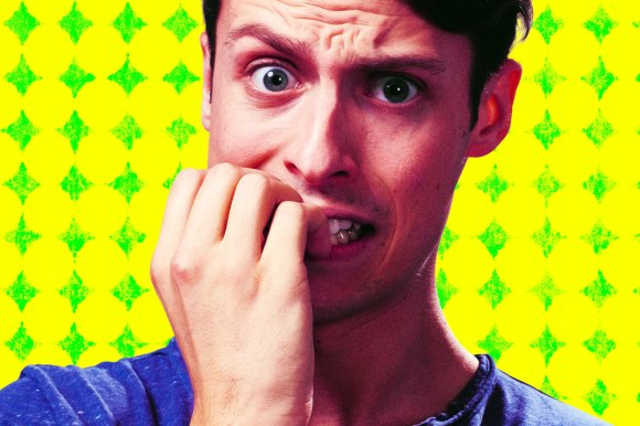 A young man chews his nails with an anxious worried look on his face over a yellow background.