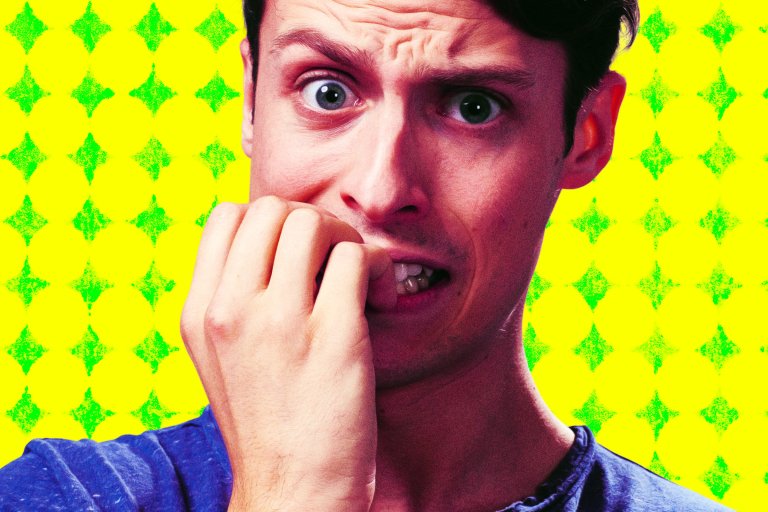 A young man chews his nails with an anxious worried look on his face over a yellow background.