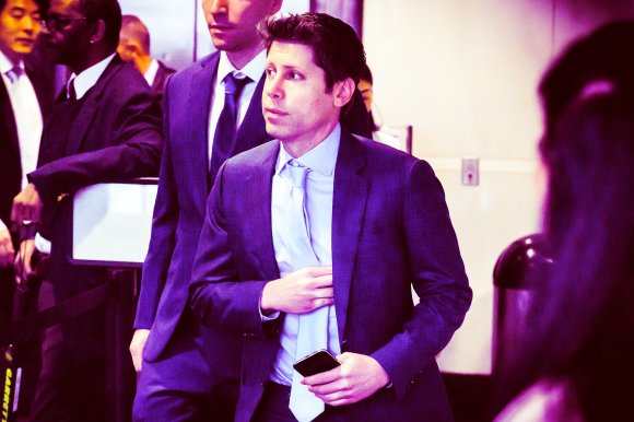 OpenAI CEO Sam Altman is shown in a light blue shirt and matching tie, holding a smartphone in his right hand and adjusting his jacket with his left hand.