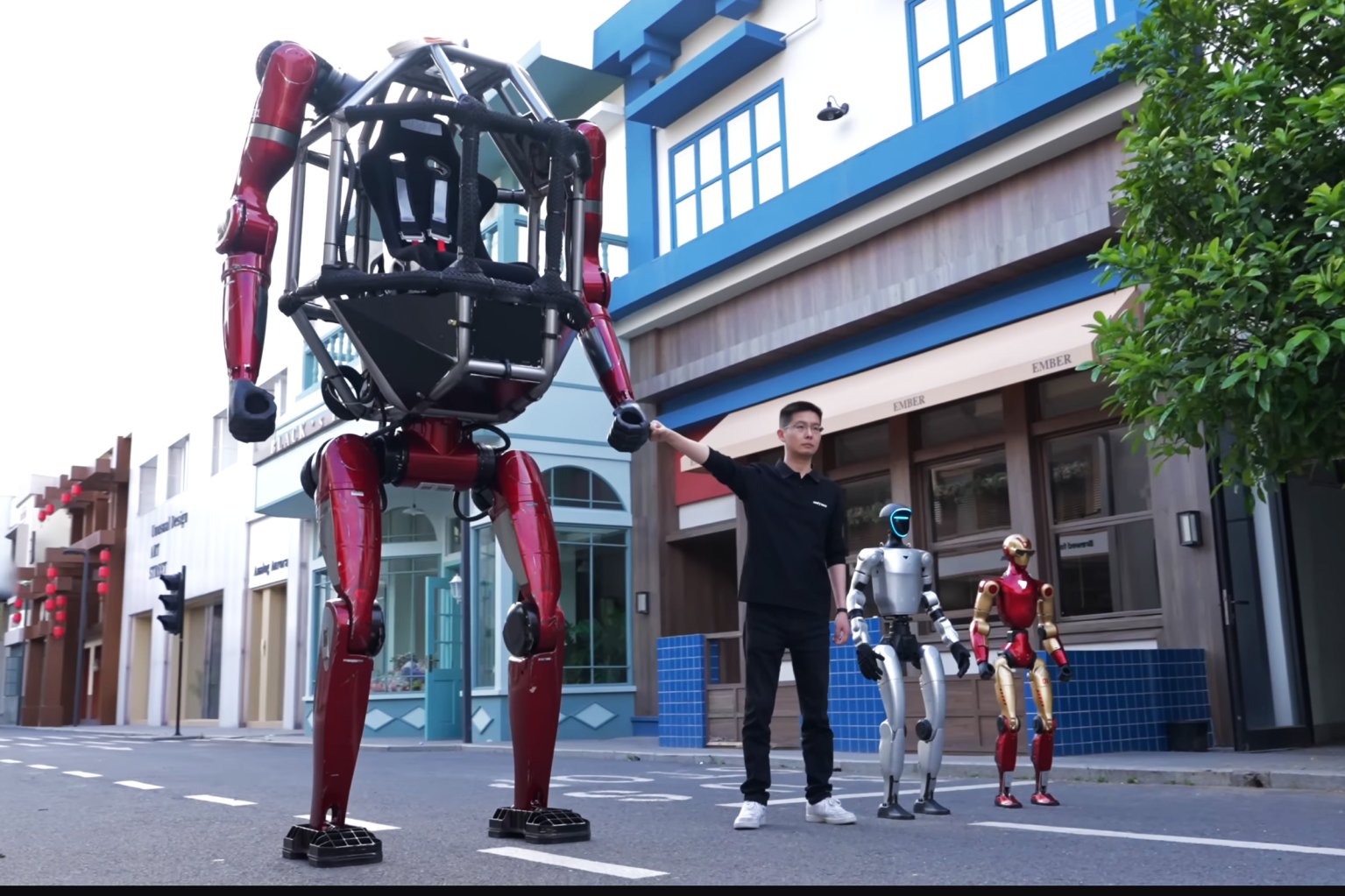 A man dressed in black is standing on a street holding the hand of a large red robot with a skeletal frame and no visible head. Next to him are two smaller humanoid robots, one silver with a blue-lit face and the other red and gold.