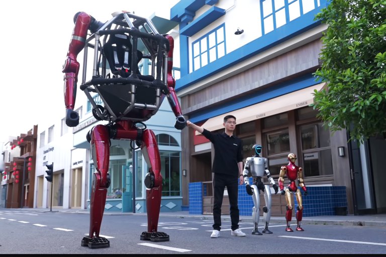 A man dressed in black is standing on a street holding the hand of a large red robot with a skeletal frame and no visible head. Next to him are two smaller humanoid robots, one silver with a blue-lit face and the other red and gold.
