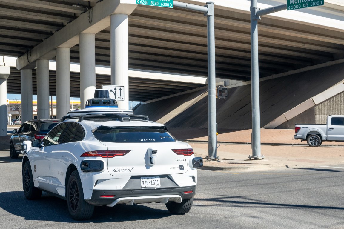 Photo shows a Waymo taxi driving under and overpass.