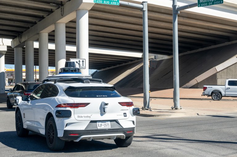 Photo shows a Waymo taxi driving under and overpass.
