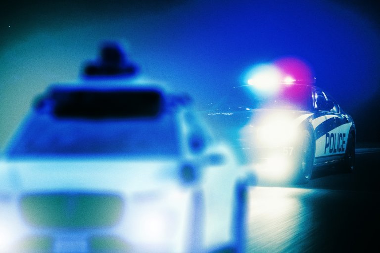 Illustration depicting a Waymo in the foreground being pursued by a police vehicle behind it.