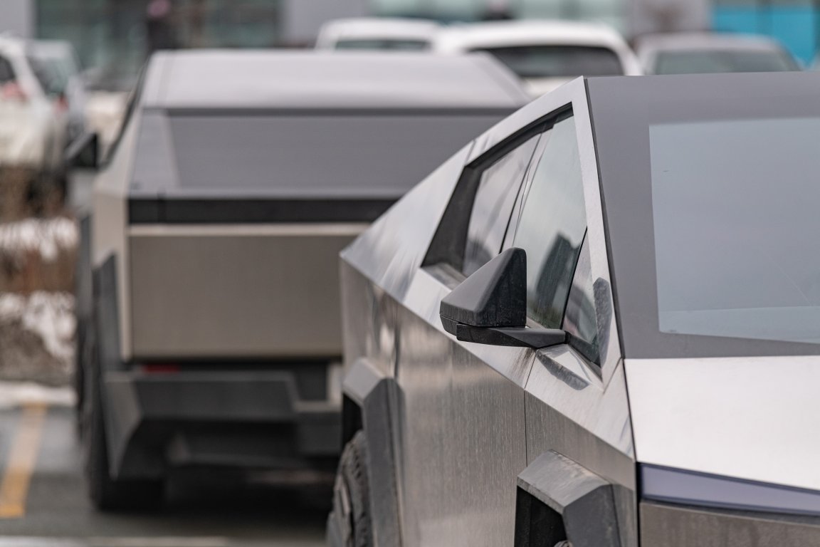 Two Tesla Cybertruck electric pickup trucks are parked in a row, showcasing their angular, futuristic stainless steel bodies and distinctive geometric design.