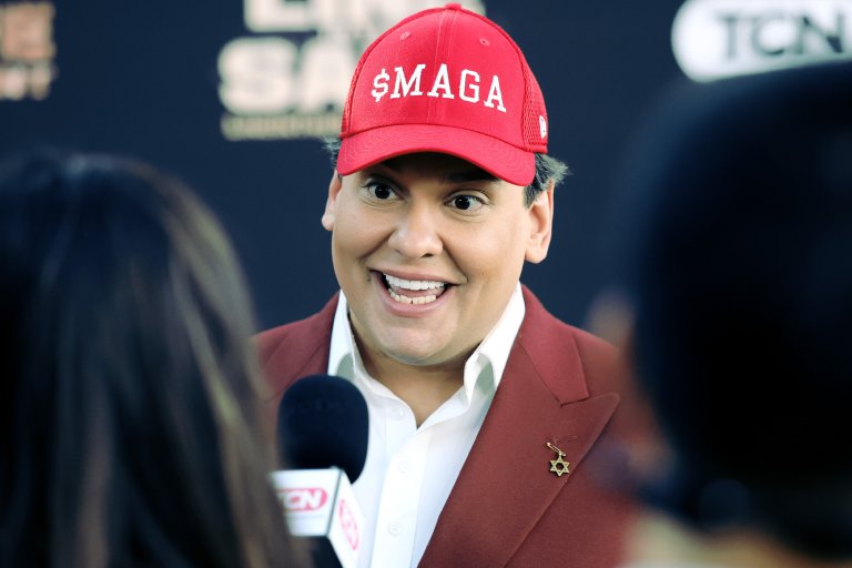 A photograph of former U.S. representative George Santos wearing a red hat embroidered with "$MAGA."